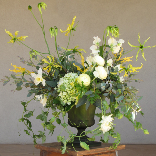 Garden centerpiece with ivory sweet peas, ivory ranunculus, ivory daffodils, yellow gloriosa lily, green hydrangea, scented geranium, gunnii eucalyptus and passion vine, arranged in a vintage green urn, by Floral Verde LLC